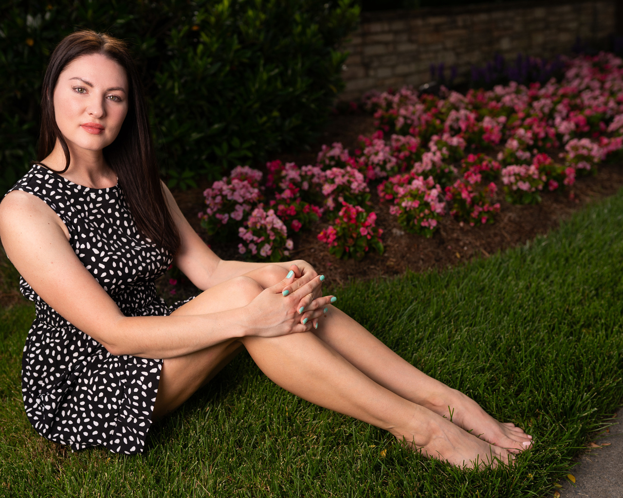 Красивая девушка в платье сидит у клумбы с цветами