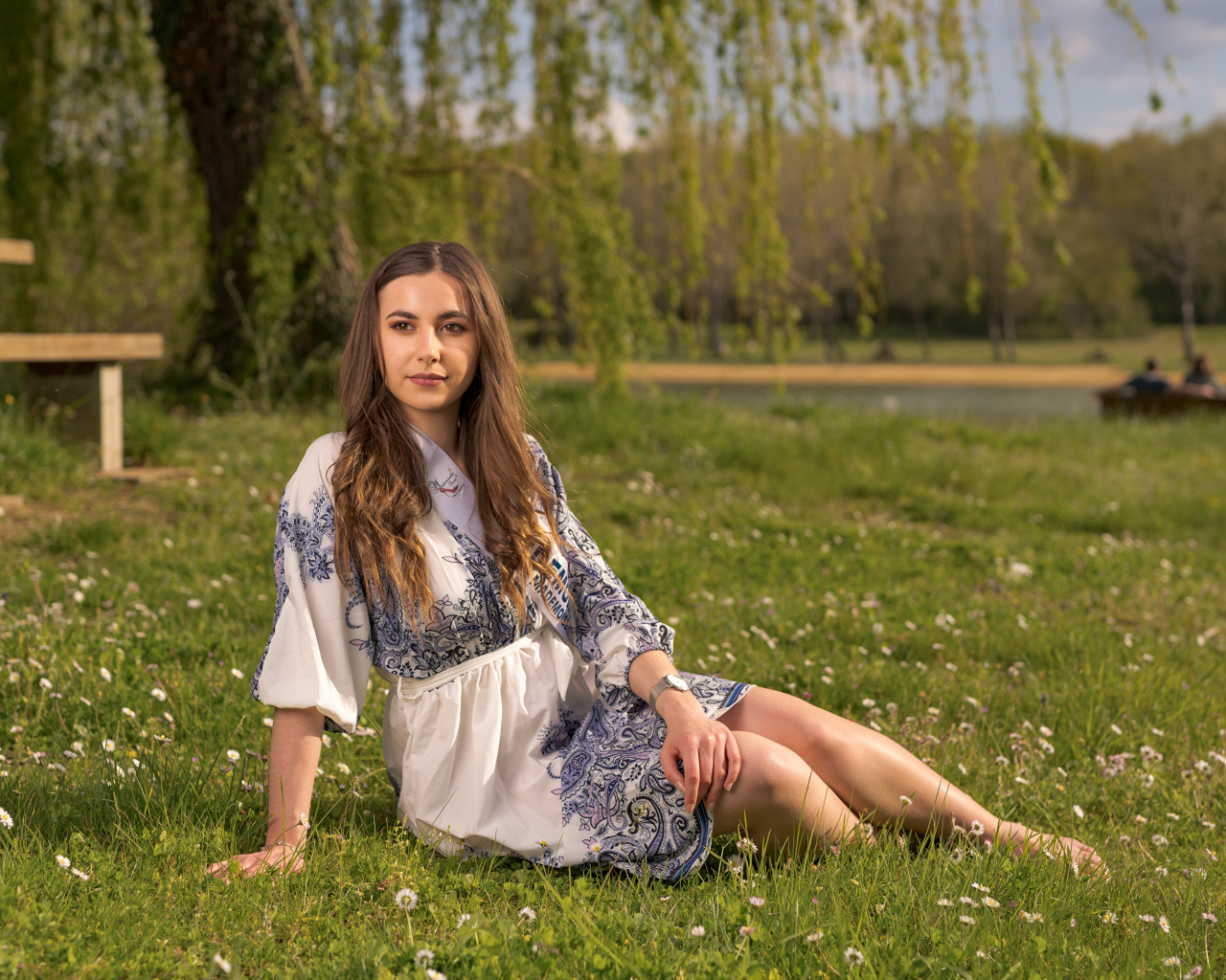 Красивая девушка в платье сидит на зеленой траве в парке