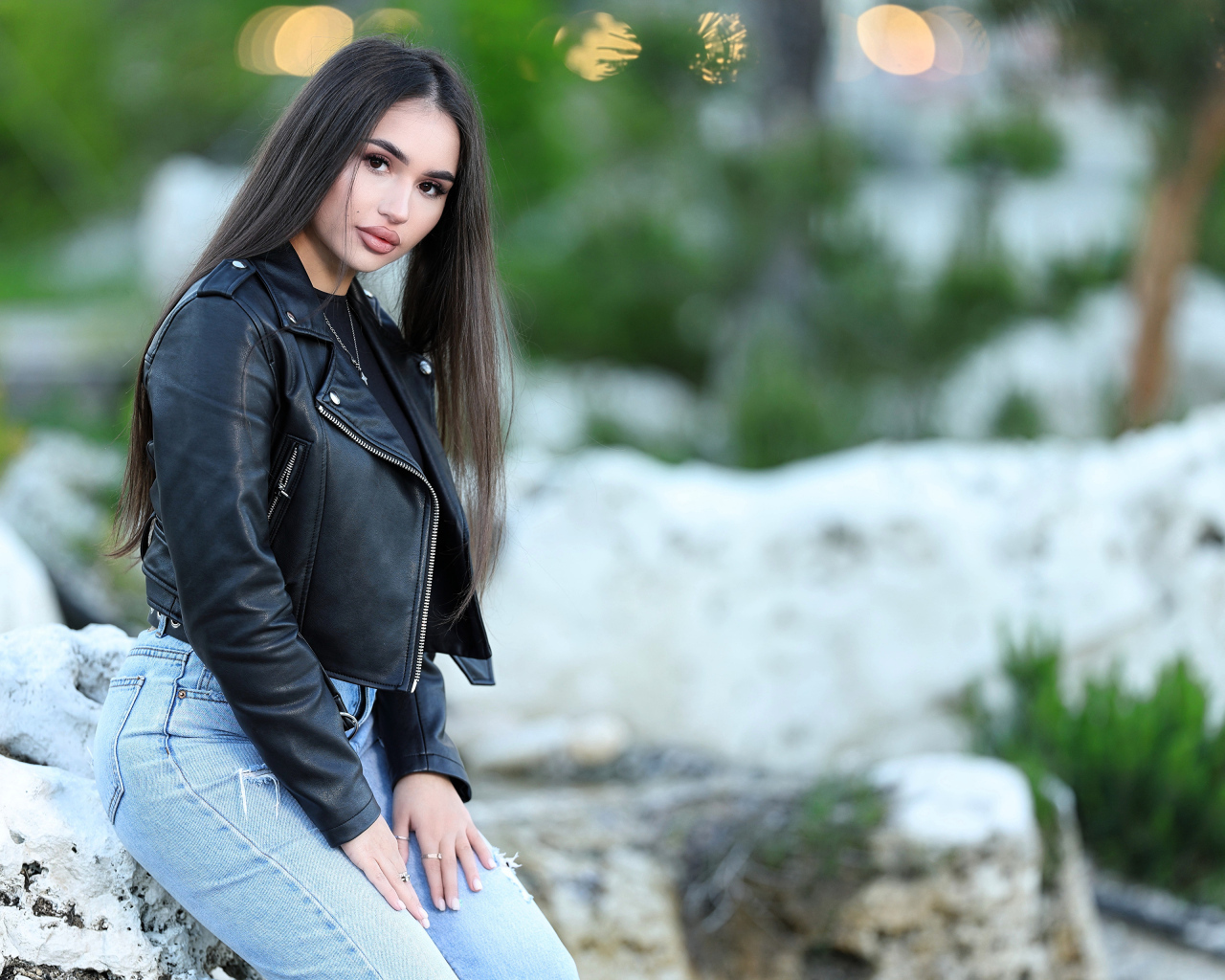 Брюнетка в черной кожаной куртке сидит на камне
