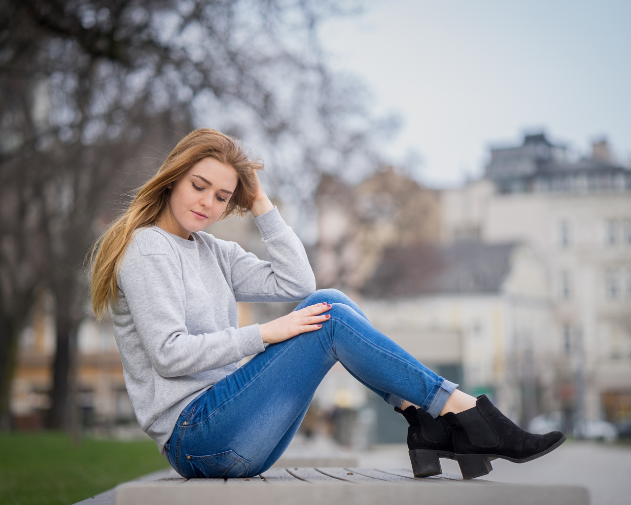 Милая девушка в синих джинсах сидит на лавке