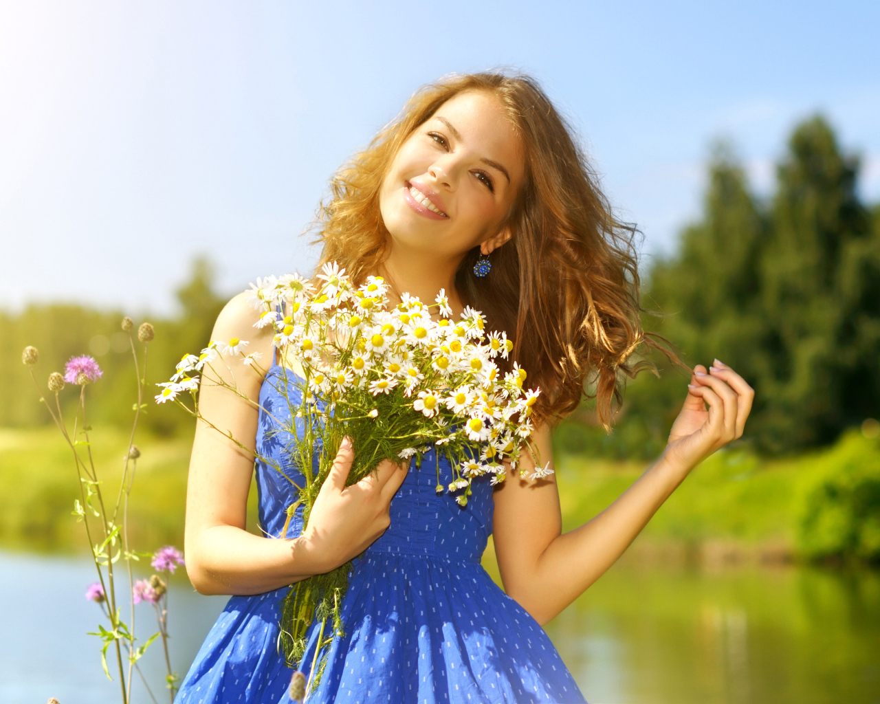 Милая улыбающаяся девушка с букетом ромашек у пруда летом