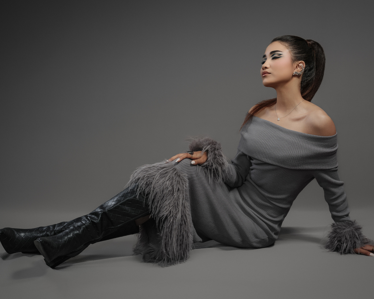 Девушка в платье и длинных черных сапогах на сером фоне