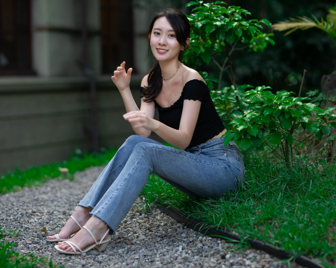 Улыбающаяся девушка азиатка сидит на зеленой траве