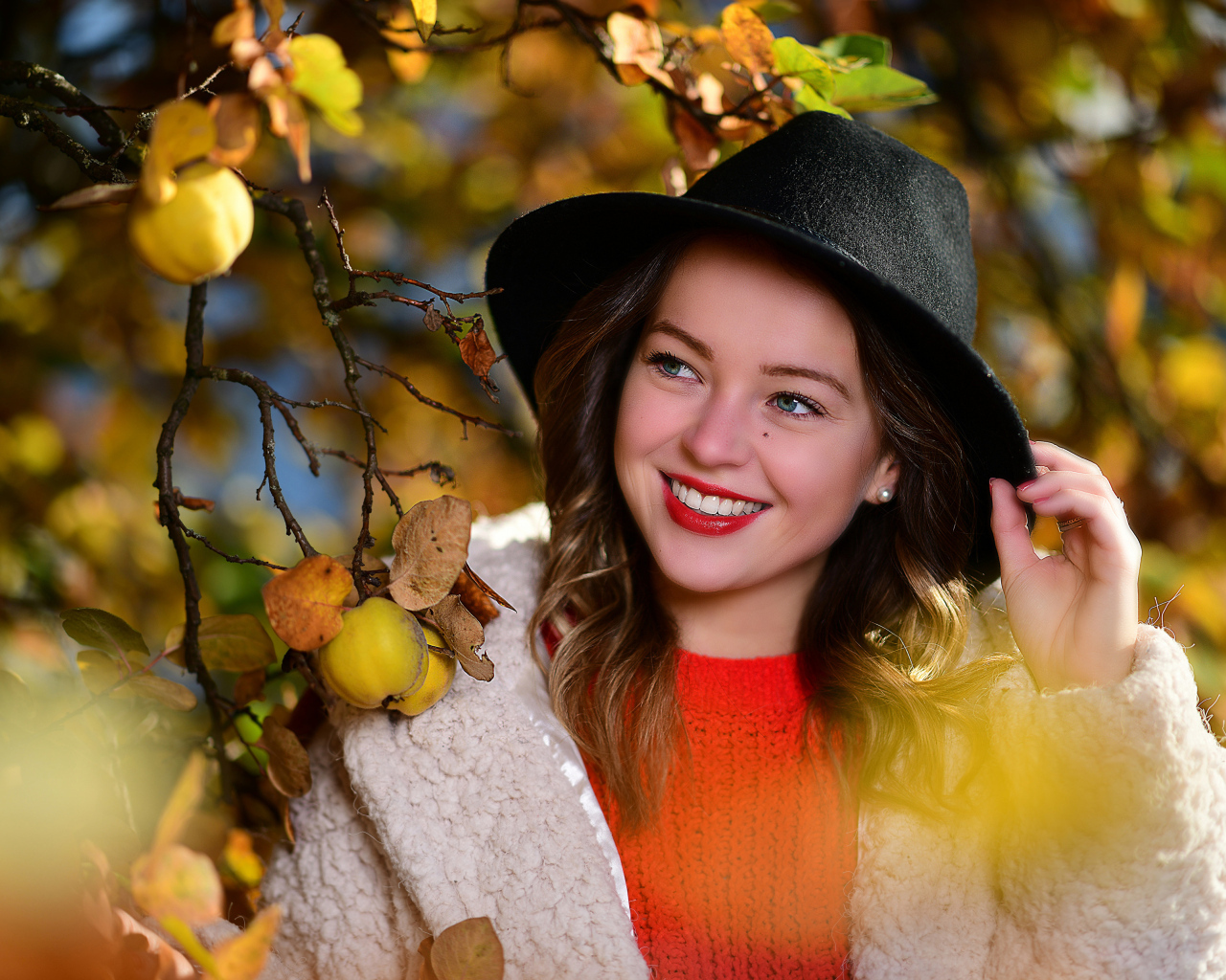 Улыбающаяся девушка в черной шляпе у дерева с яблоками