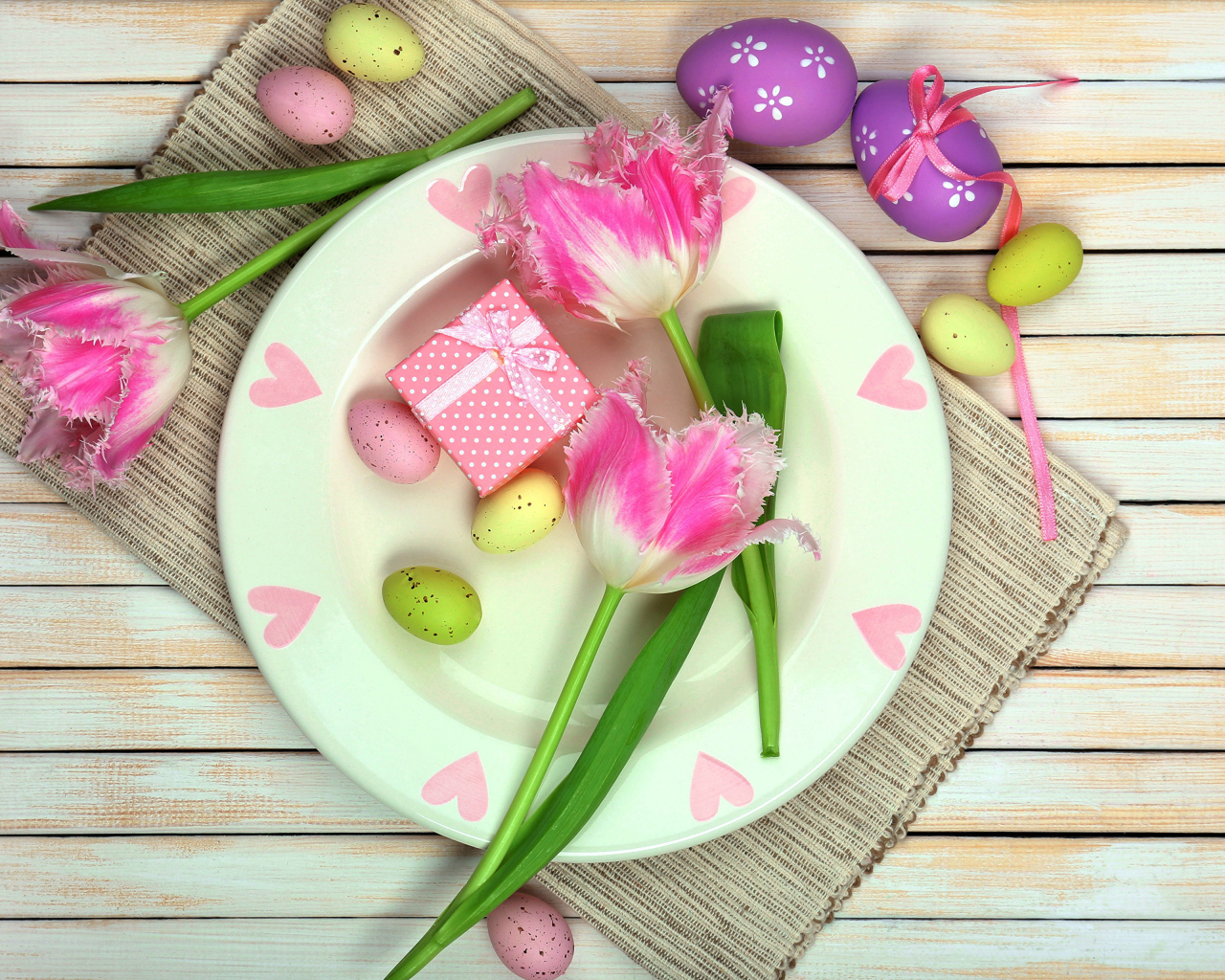 Пасхальные яйца с тюльпанами на тарелке на столе