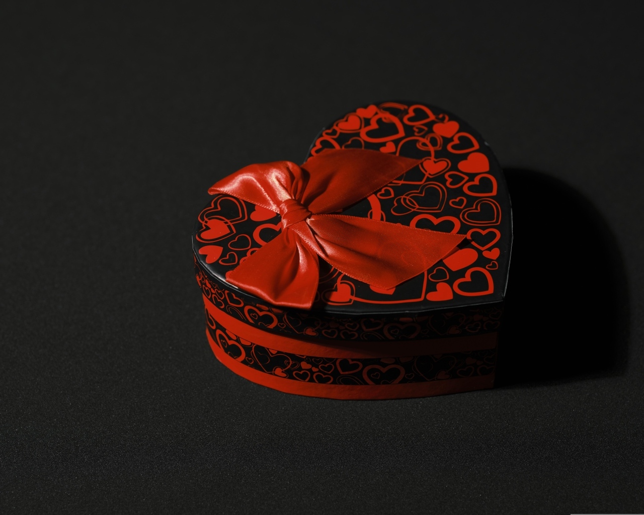 Шкатулка в форме сердца с красным бантом на черном фоне