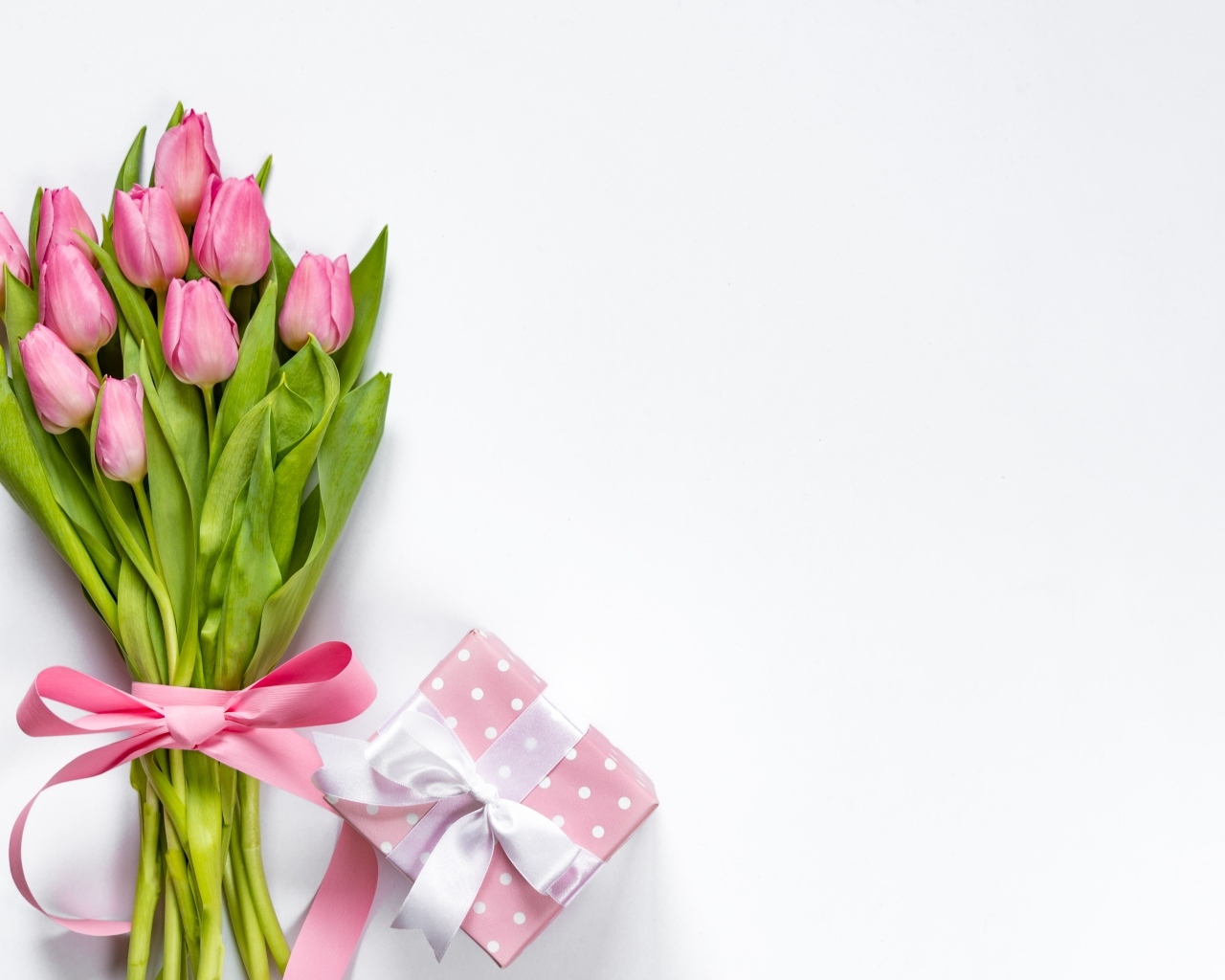 Букет розовых тюльпанов с лентой на столе с подарком