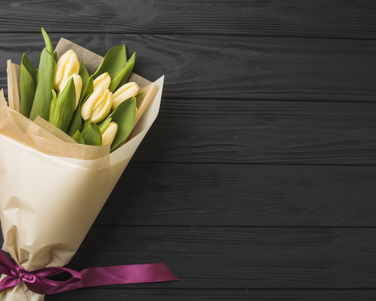 Букет желтых тюльпанов в бумаге на черном столе