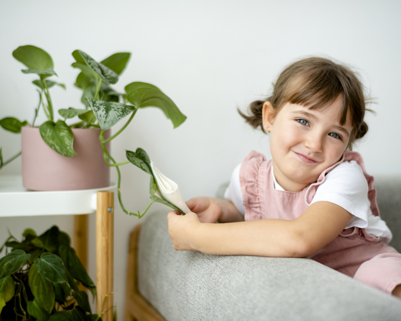 Маленькая девочка сидит на диване у цветка