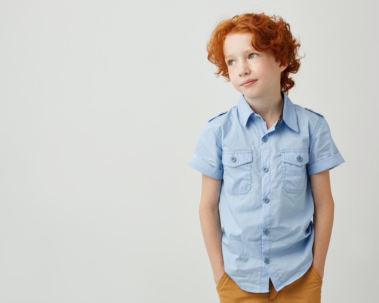 Рыжеволосый мальчик на фоне серой стены