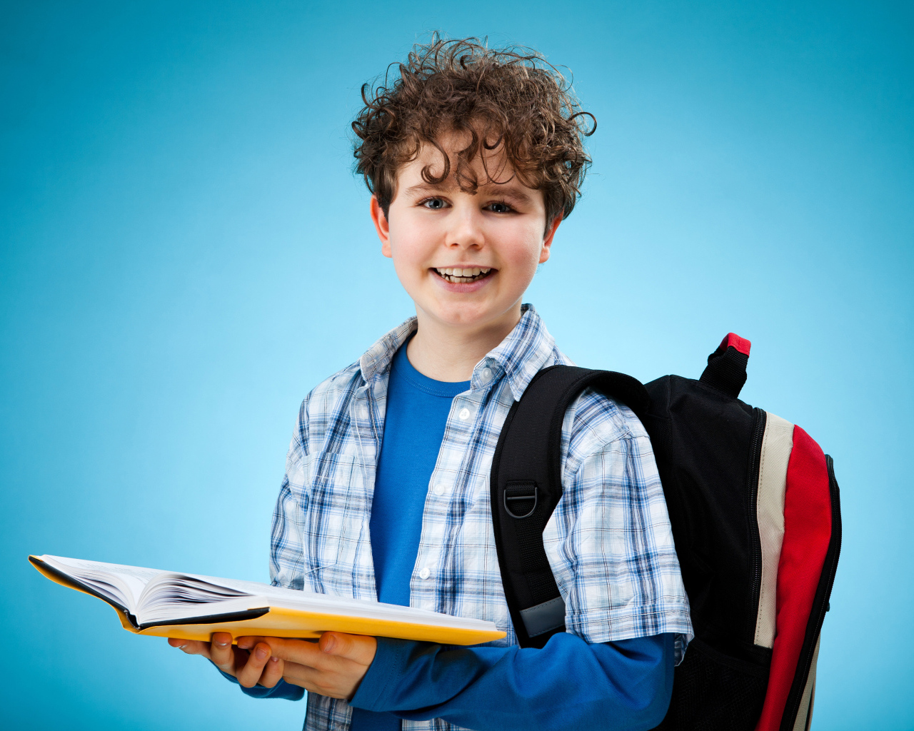 Улыбающийся школьник с книгой и портфелем