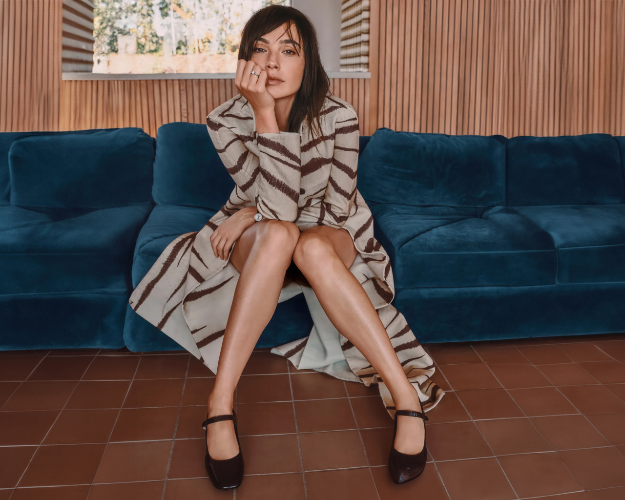 Актриса Галь Гадот в пальто сидит на диване