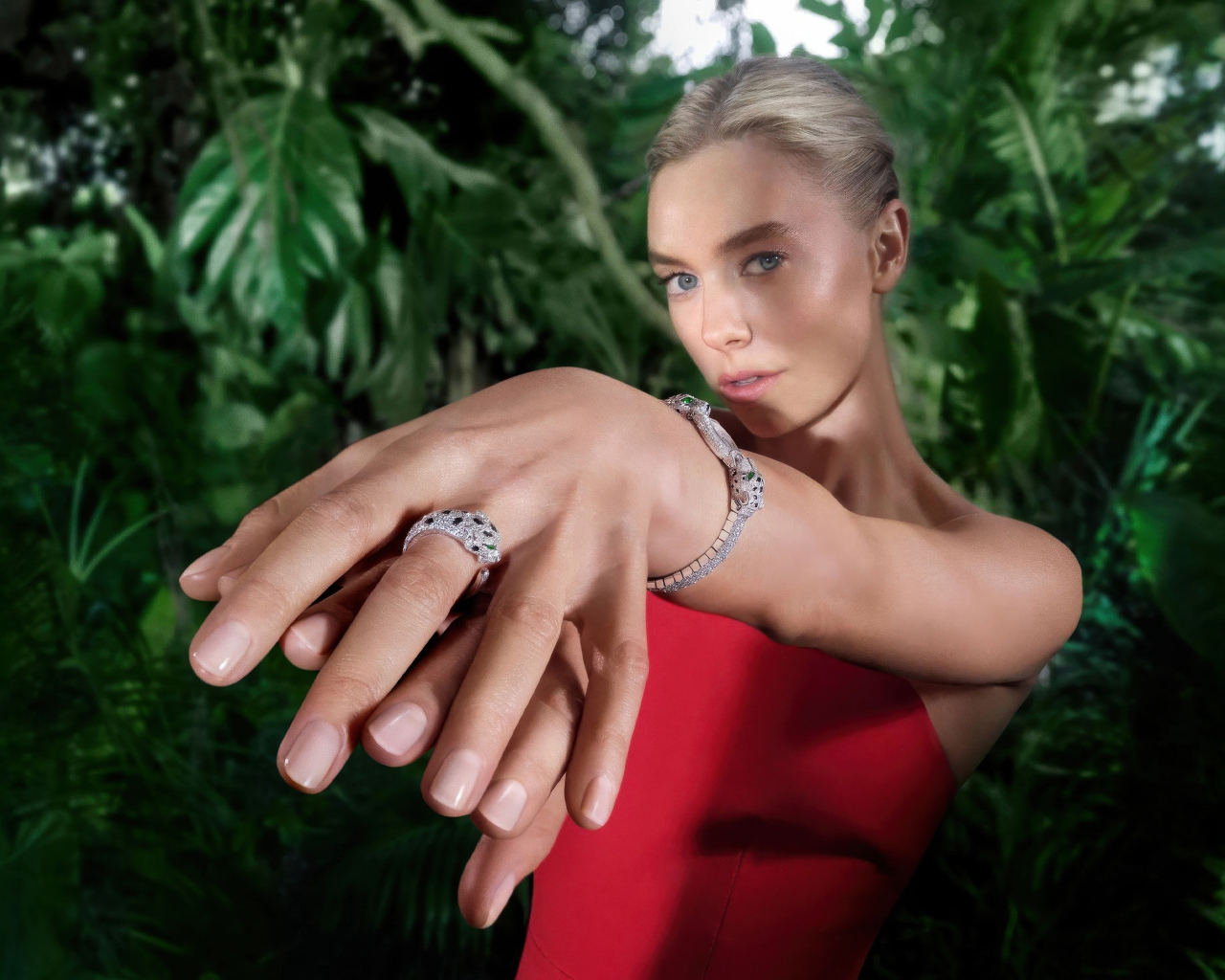Актриса Ванесса Кирби в красном платье с кольцом на руке на фоне зарослей
