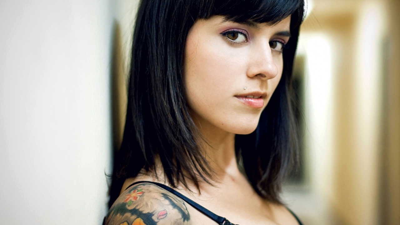 Девушка брюнетка с пирсингом в губе и татуировкой на плече