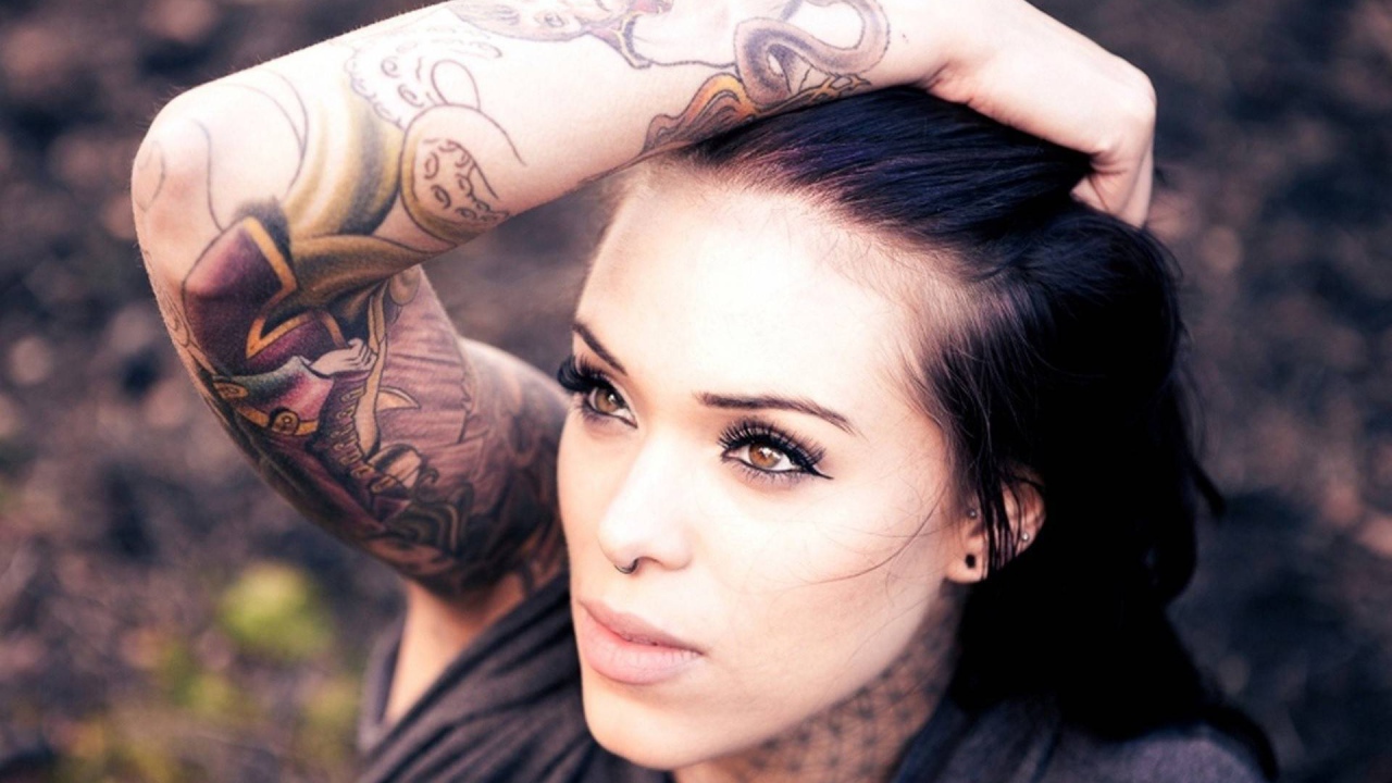 Девушка брюнетка с пирсингом в носу и татуировкой на руке