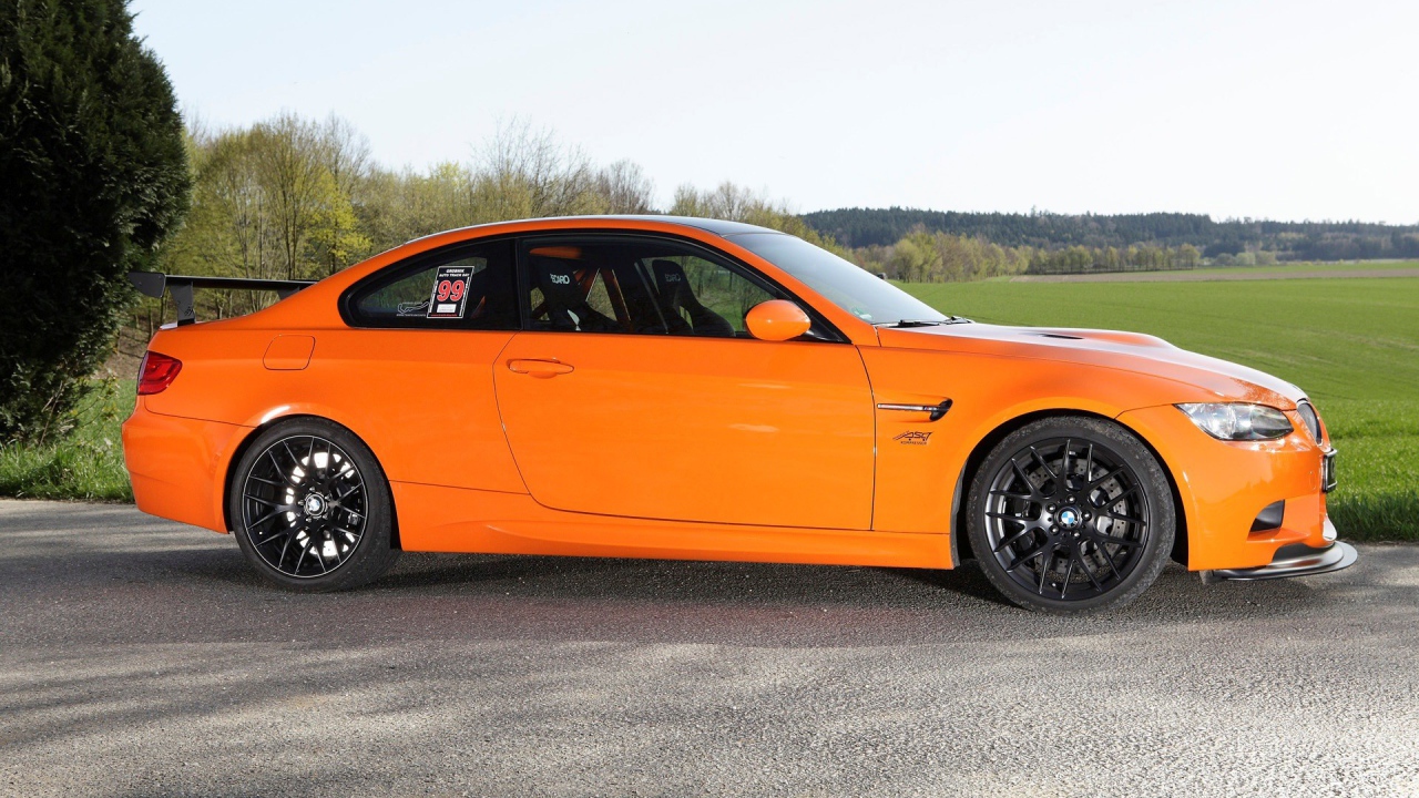 Оранжевый BMW M3 GTS на фоне зеленого поля