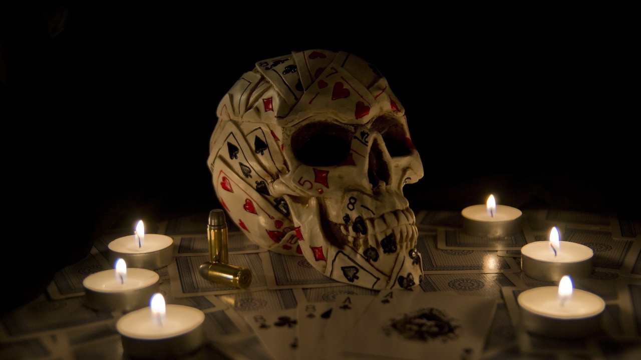 Череп из игровых карт среди свечей