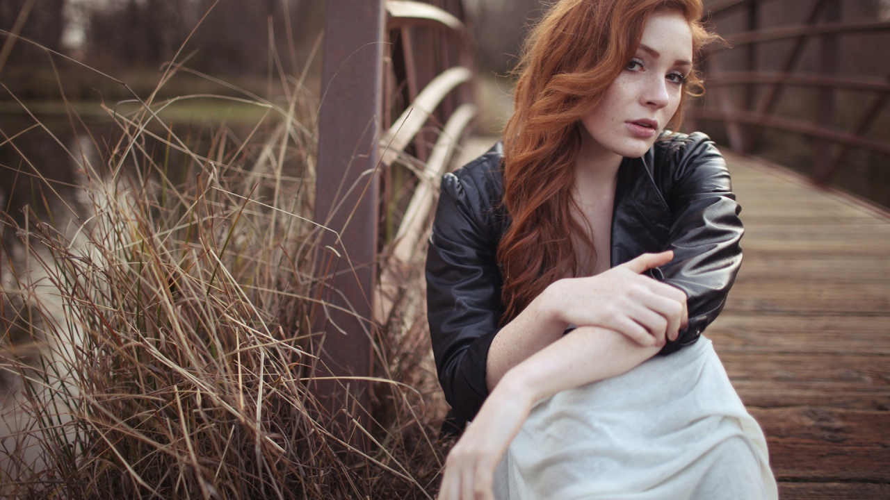 Девушка в кожаной куртке сидит у деревянного моста