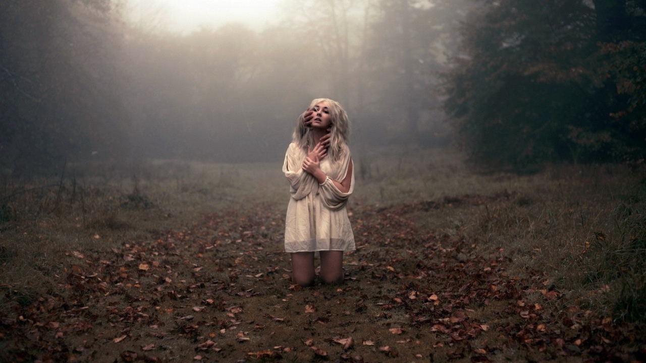 Блондинка в белом платье стоит на коленях среди леса