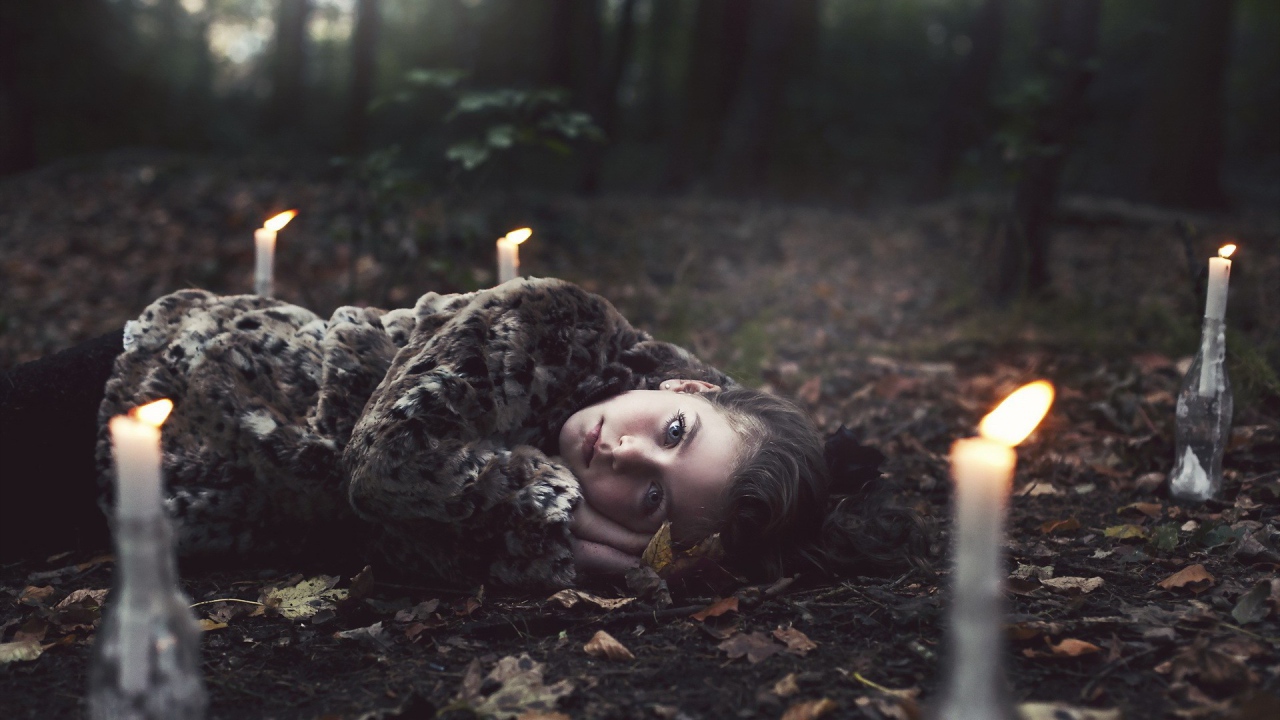 Девушка лежит среди свечей в лесу