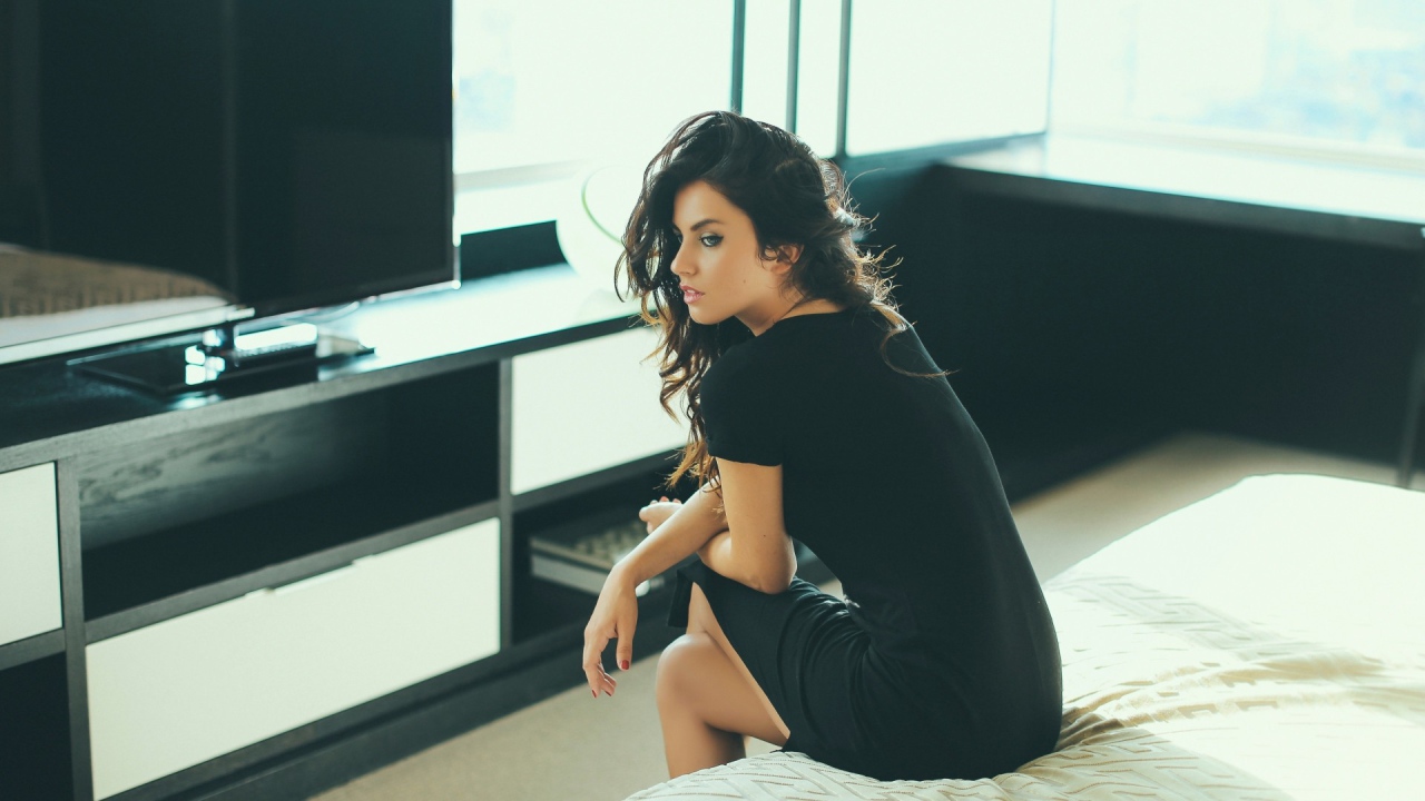 Девушка сидит на кровати перед телевизором