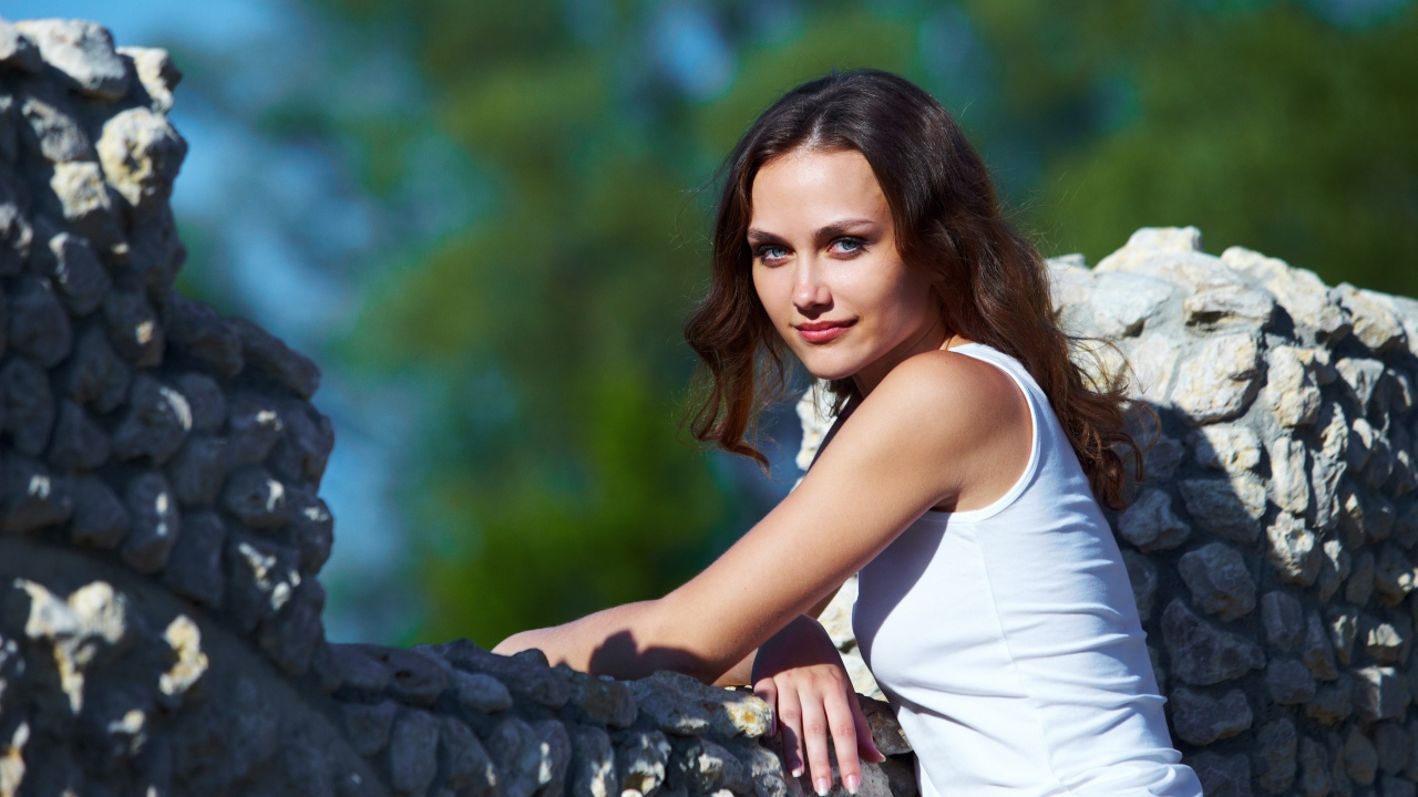 Девушка стоит у забора из камня