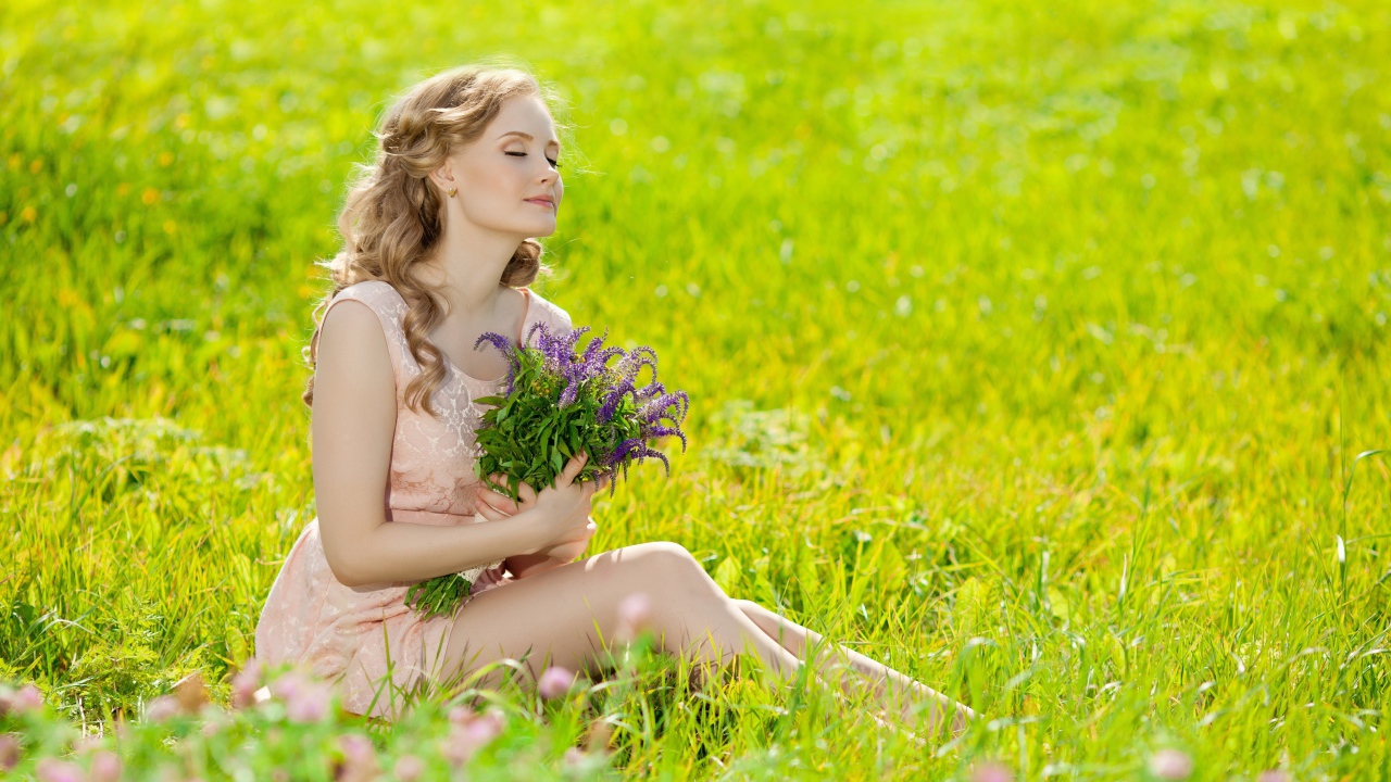 Девушка с букетом сидит на зеленой траве