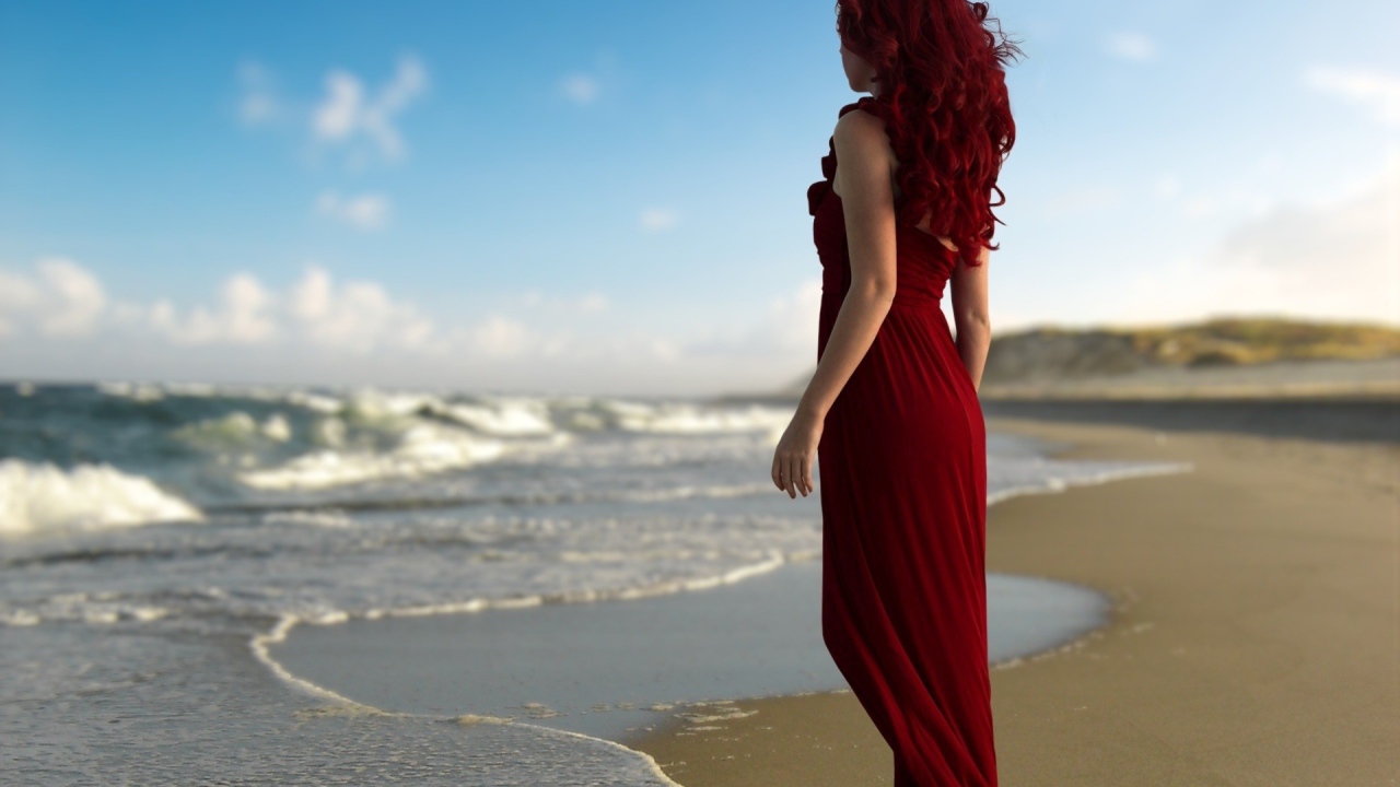 Girl with red hair in a red dress on the beach