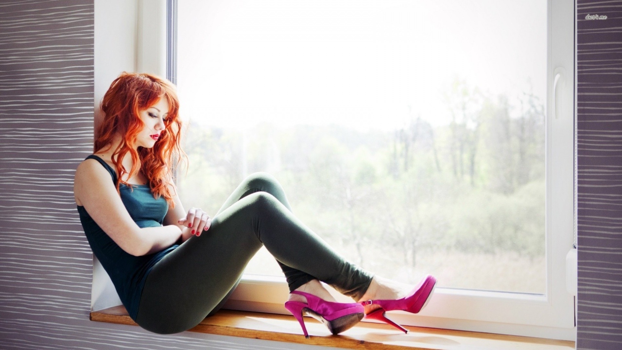 Рыжая девушка в розовых туфлях сидит на окне