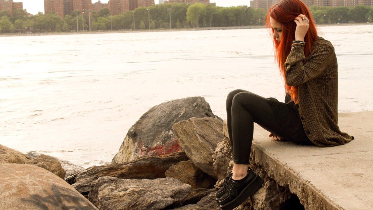 Рыжая девушка сидит на плитах набережной