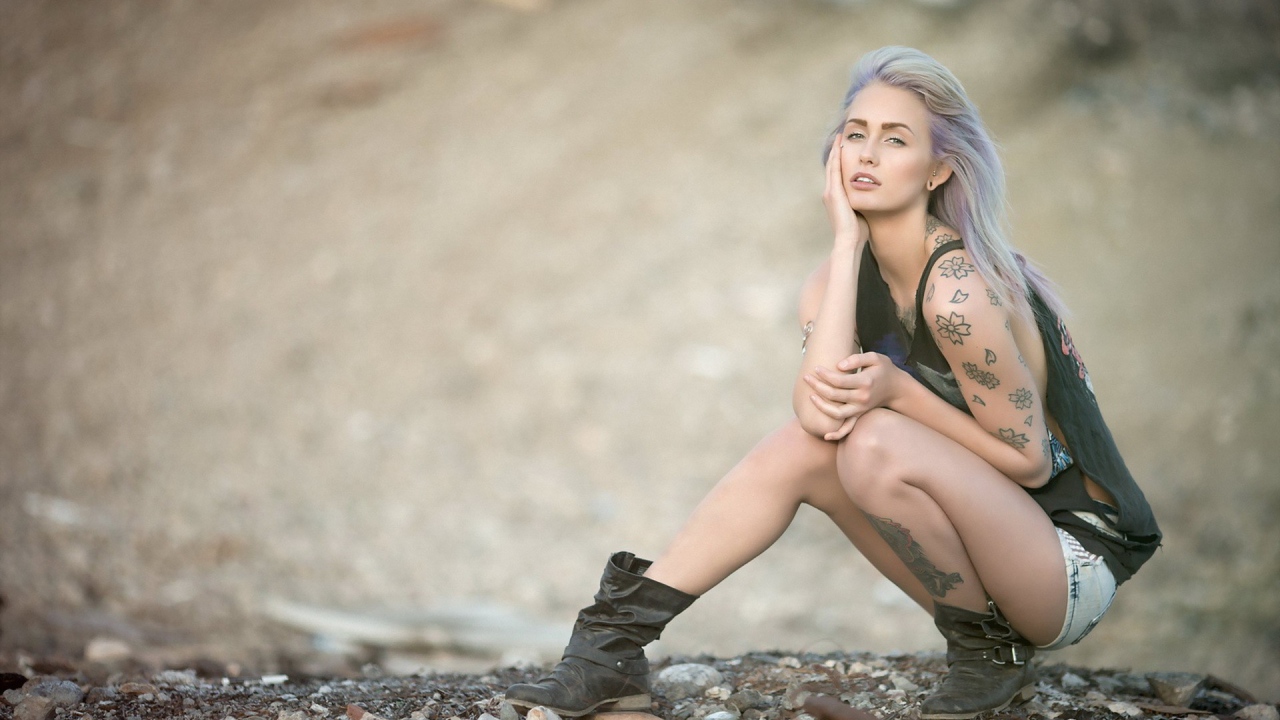 Девушка с татуировками в форме цветов сидит на корточках