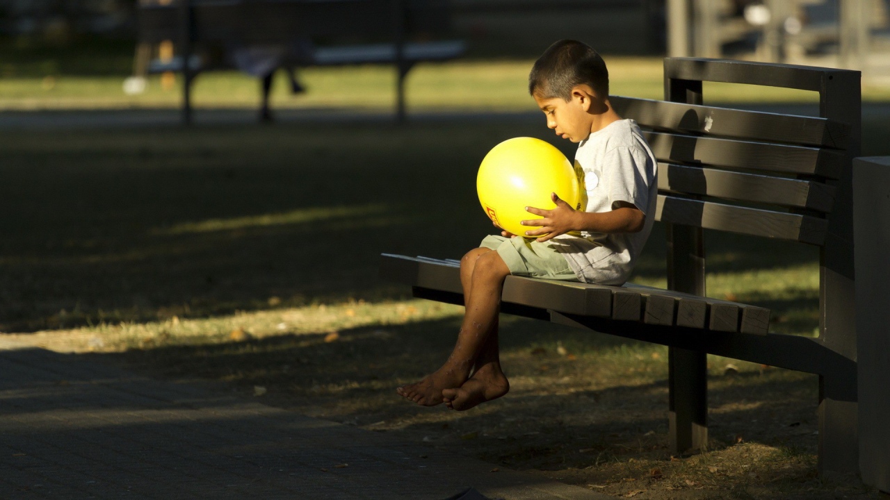 Мальчик сидит на скамье с шариком в руках