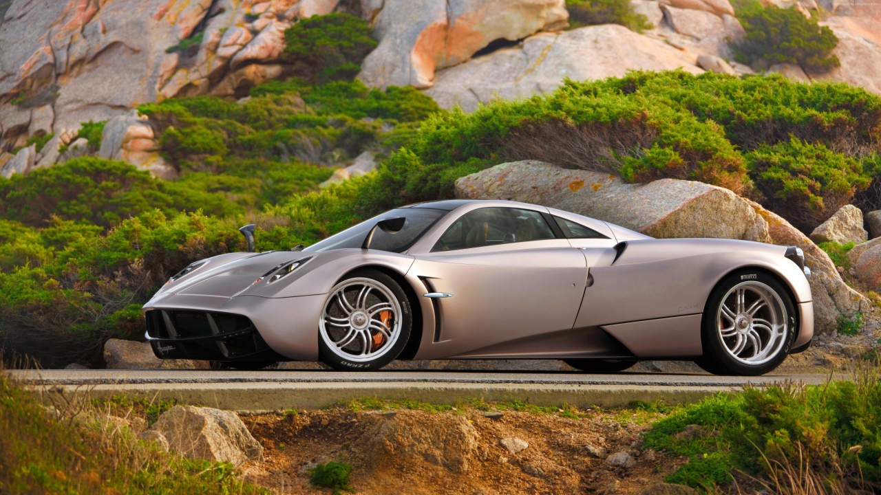 Серебристый быстрый автомобиль  Pagani Huayra на трассе у скалы