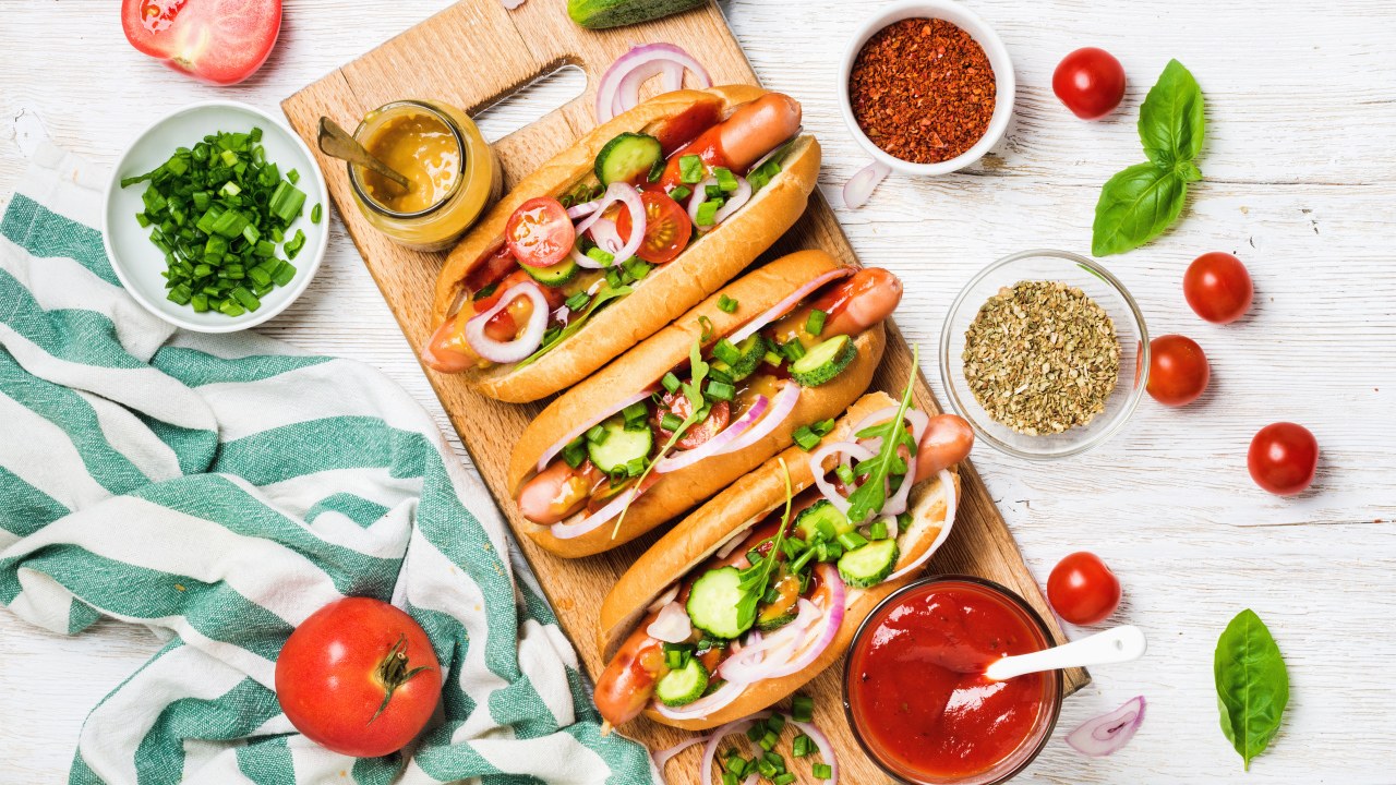 Аппетитные хотдоги на разделочной доске с овощами
