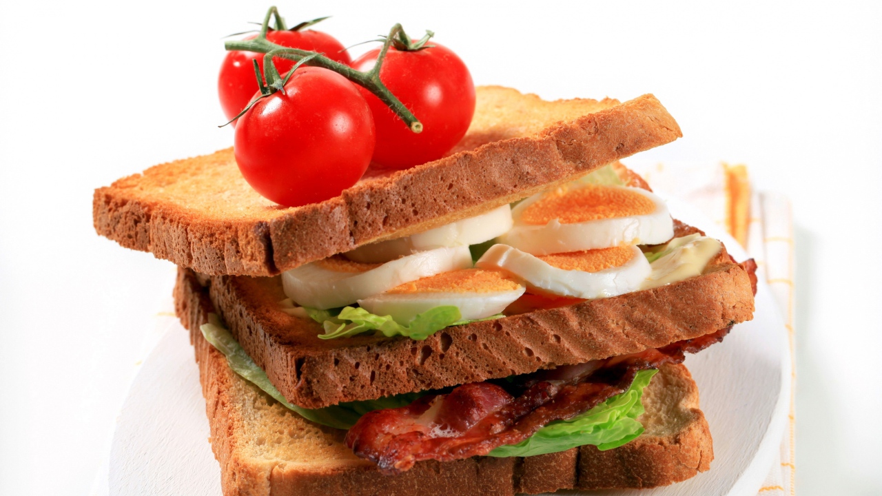 Сэндвич с беконом, яйцами и овощами на белом фоне