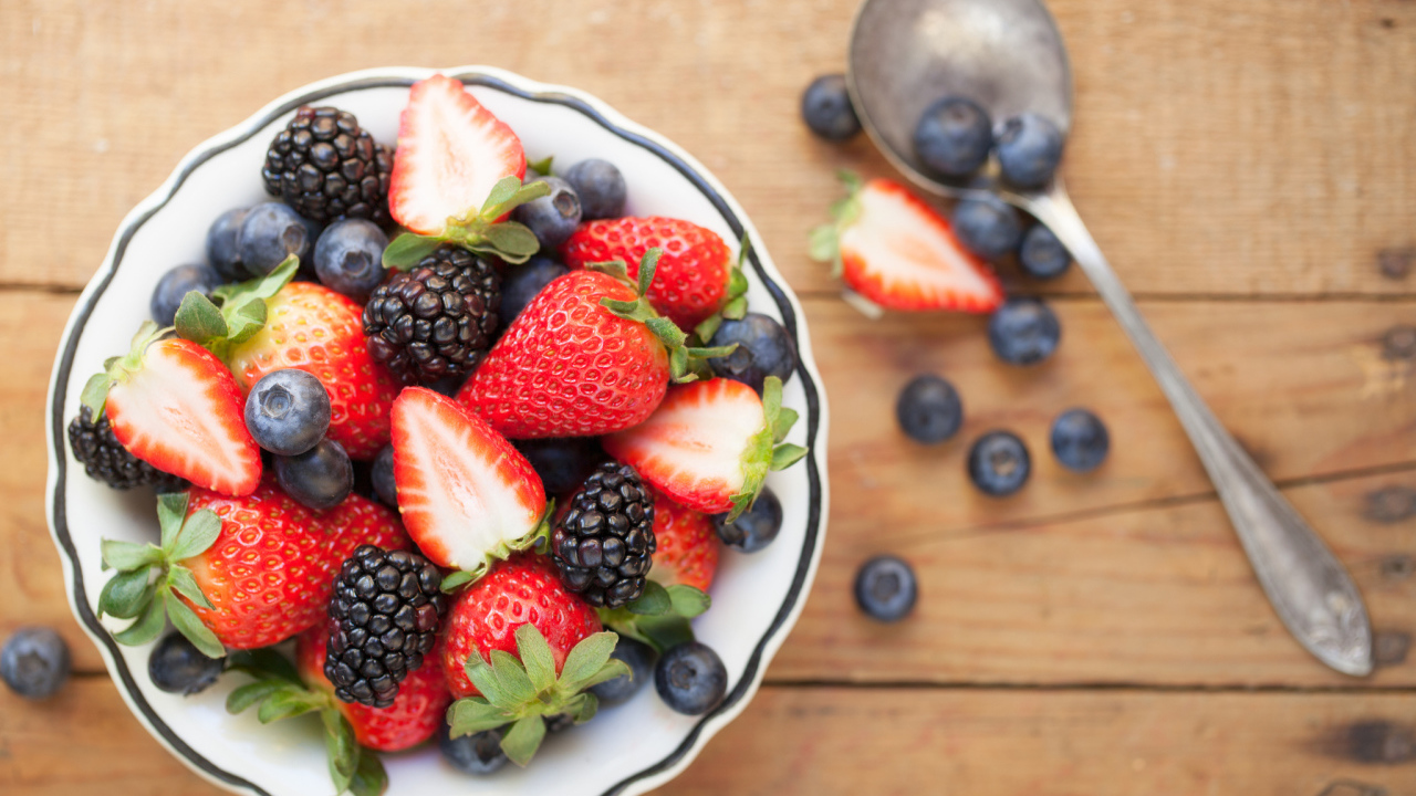 Свежие ягоды клубники, черники и ежевики в тарелке на деревянном столе