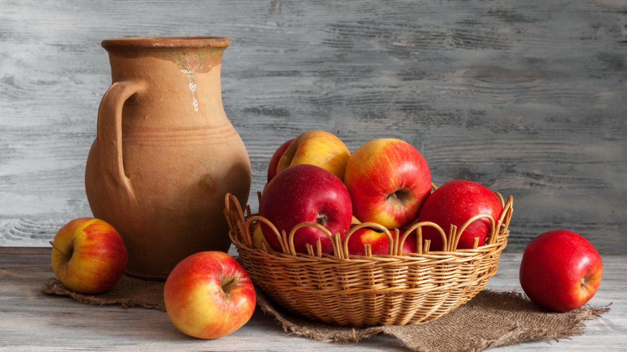 Красные яблоки в корзинке на столе с кувшином