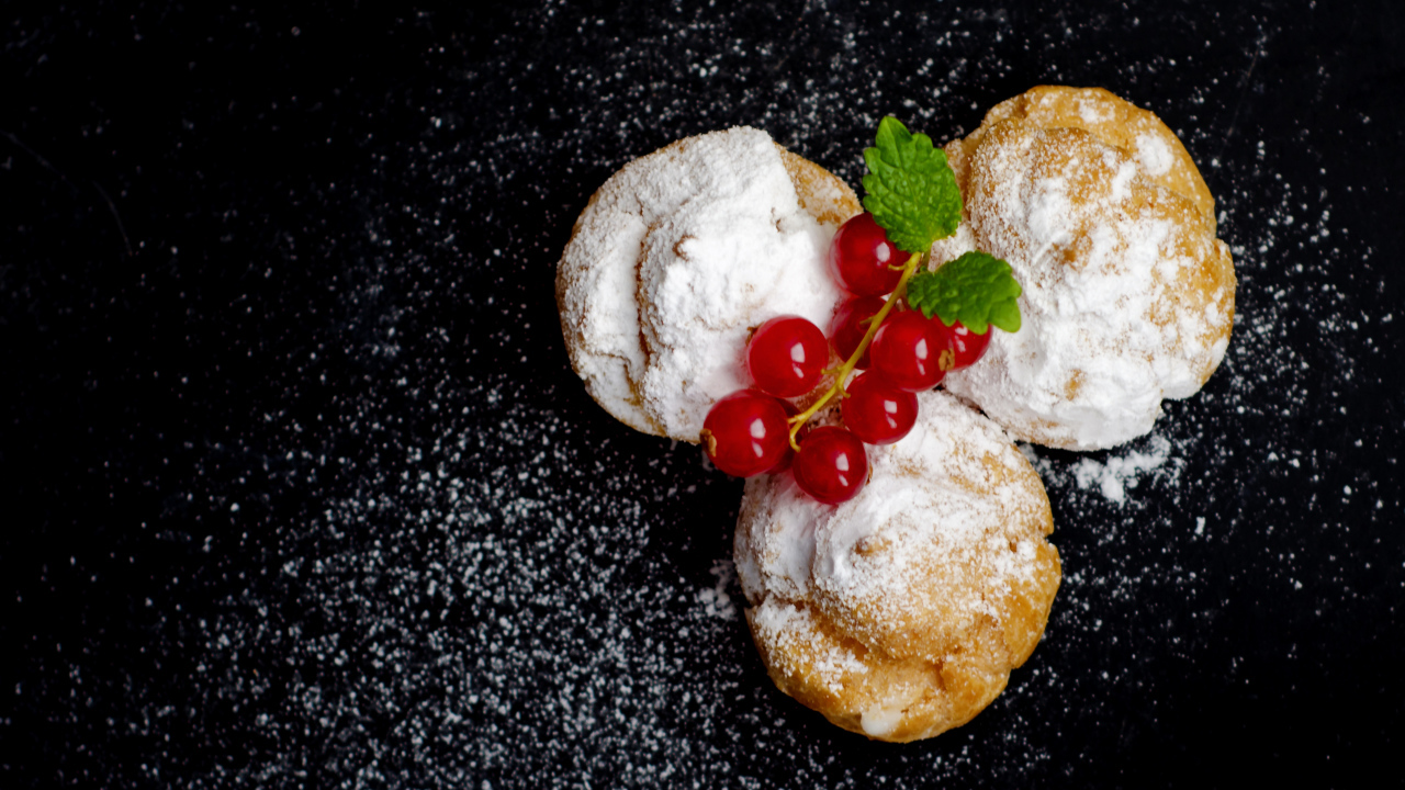 Три пирожных с сахарной пудрой и красной смородиной на черном фоне