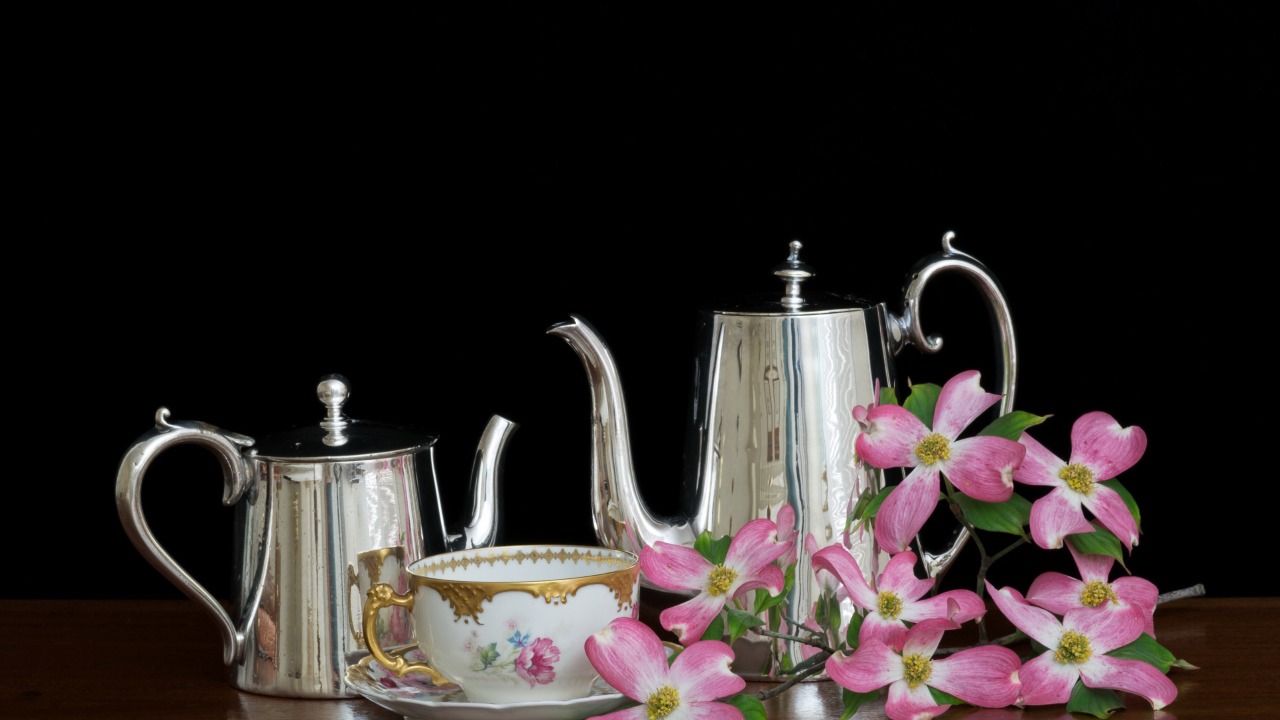 Чайники с чашкой с цветами на столе на черном фоне