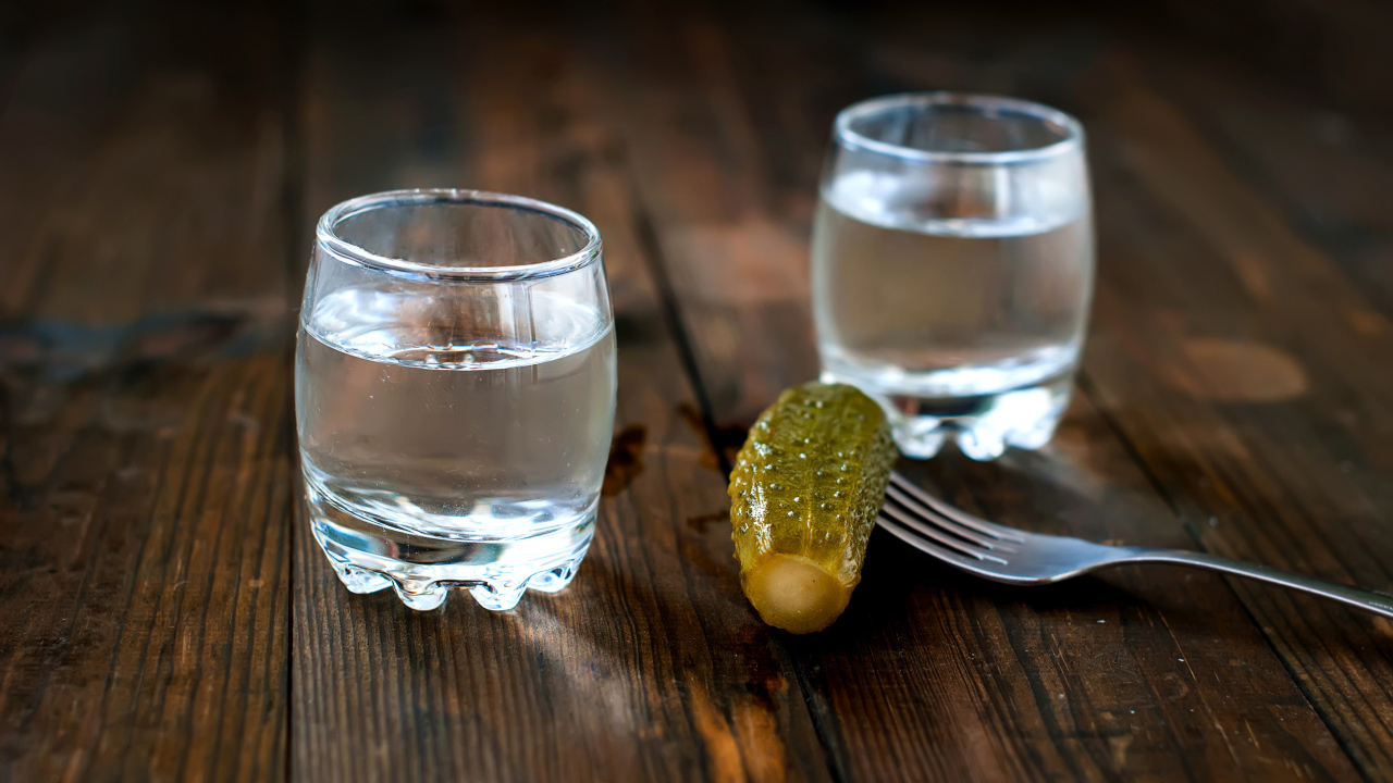 Две рюмки водки и соленый огурец на столе