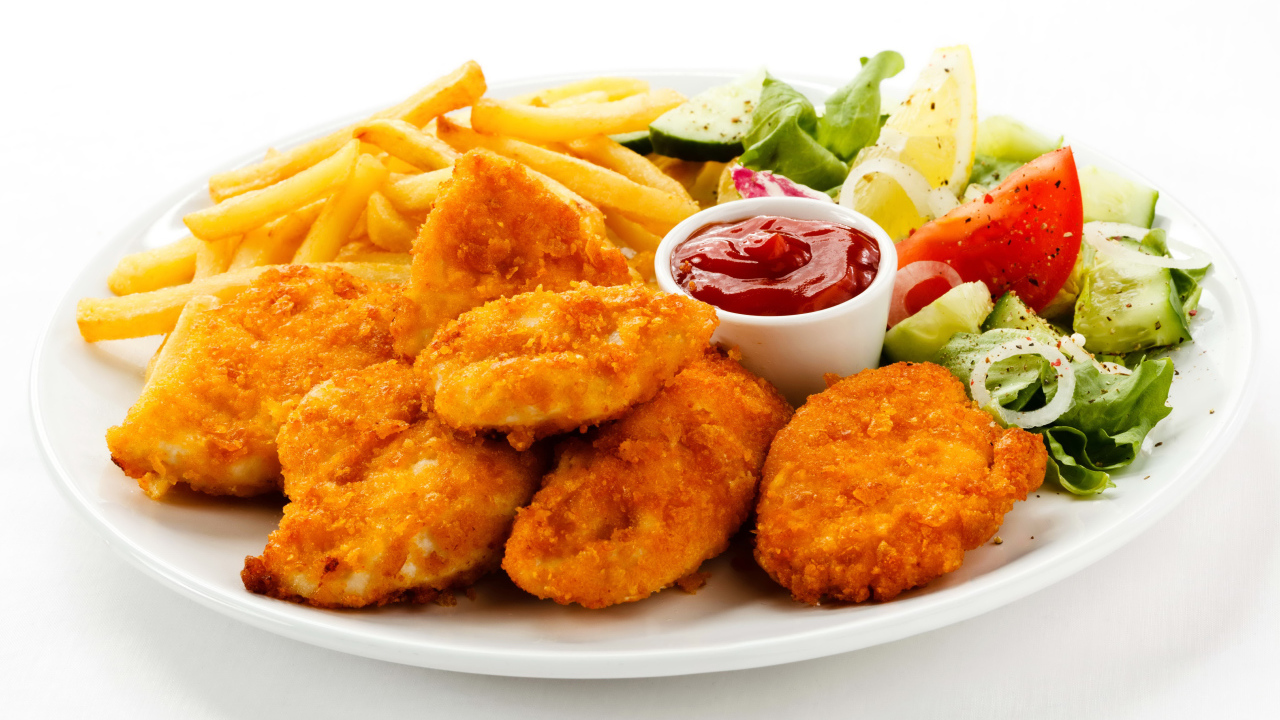 Куриные наггетсы с кетчупом, картофелем фри и салатом на белой тарелке