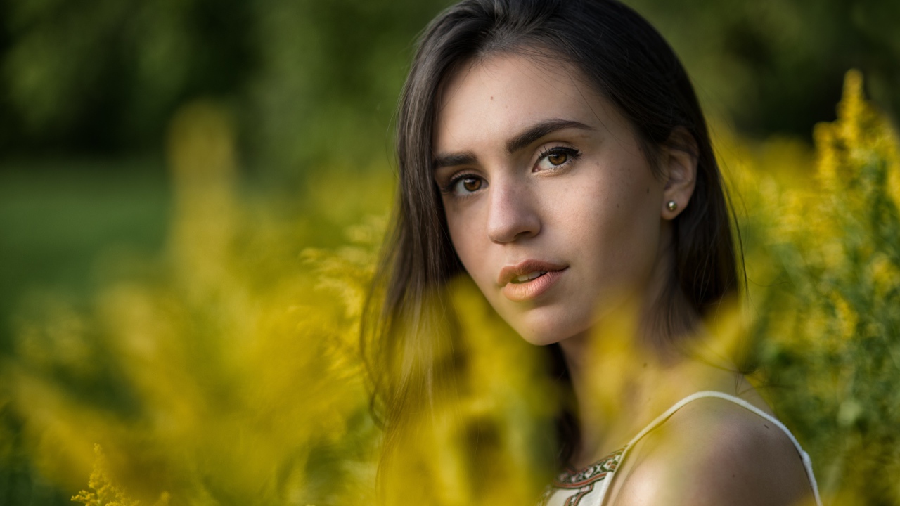 Красивая девушка с нежным взглядом сидит у желтых цветов