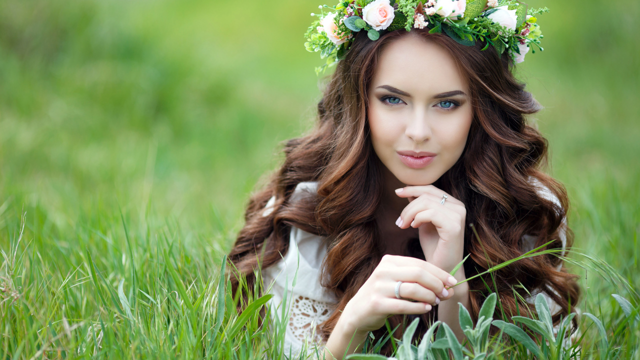 Красивая девушка шатенка с венком на голове лежит на зеленой траве