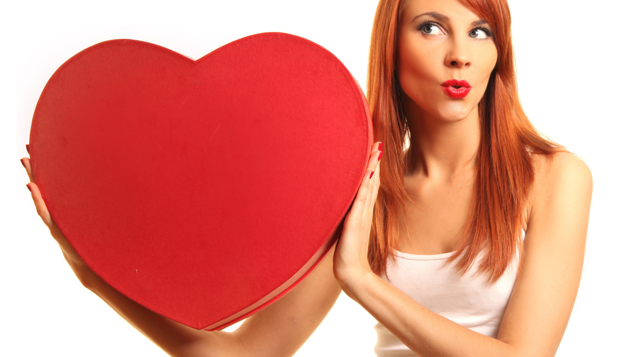 Рыжеволосая девушка с большим красным сердцем в руках на белом фоне