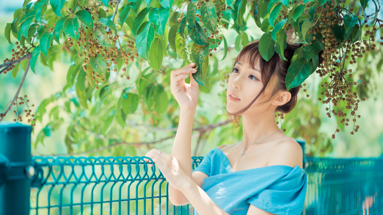 Молодая красивая девушка азиатка стоит у ветки с зелеными листьями