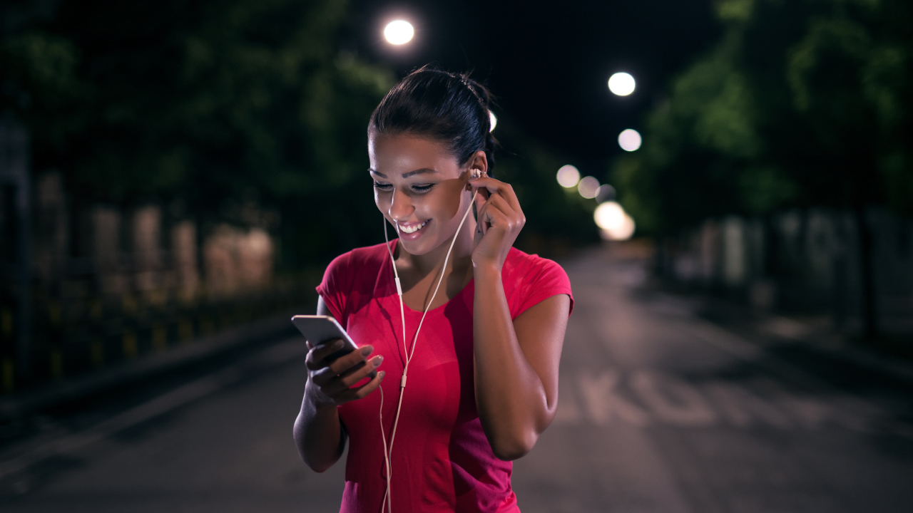 Молодая улыбающаяся девушка в наушниках с телефоном в руках