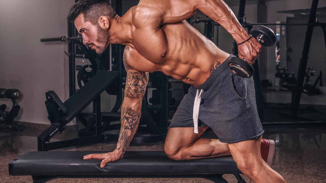 Мускулистый мужчина занимается в спортзале с гантелей