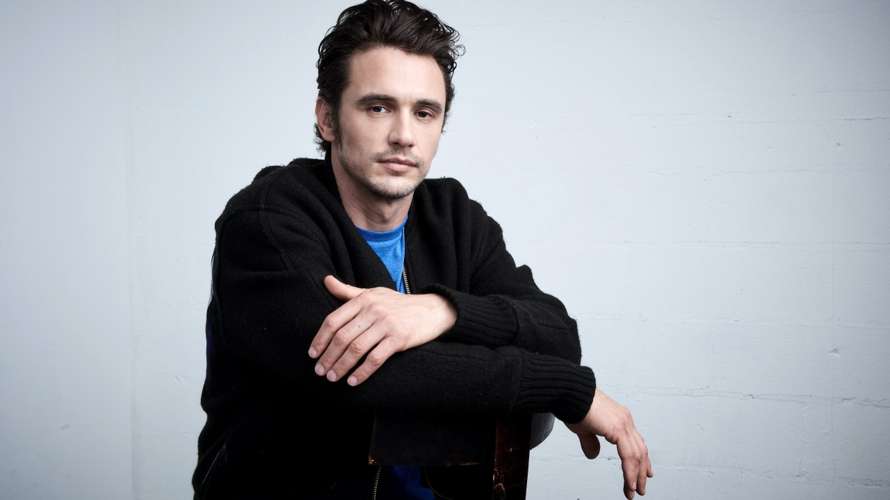 Актер Джеймс Франко в черной кофте на сером фоне