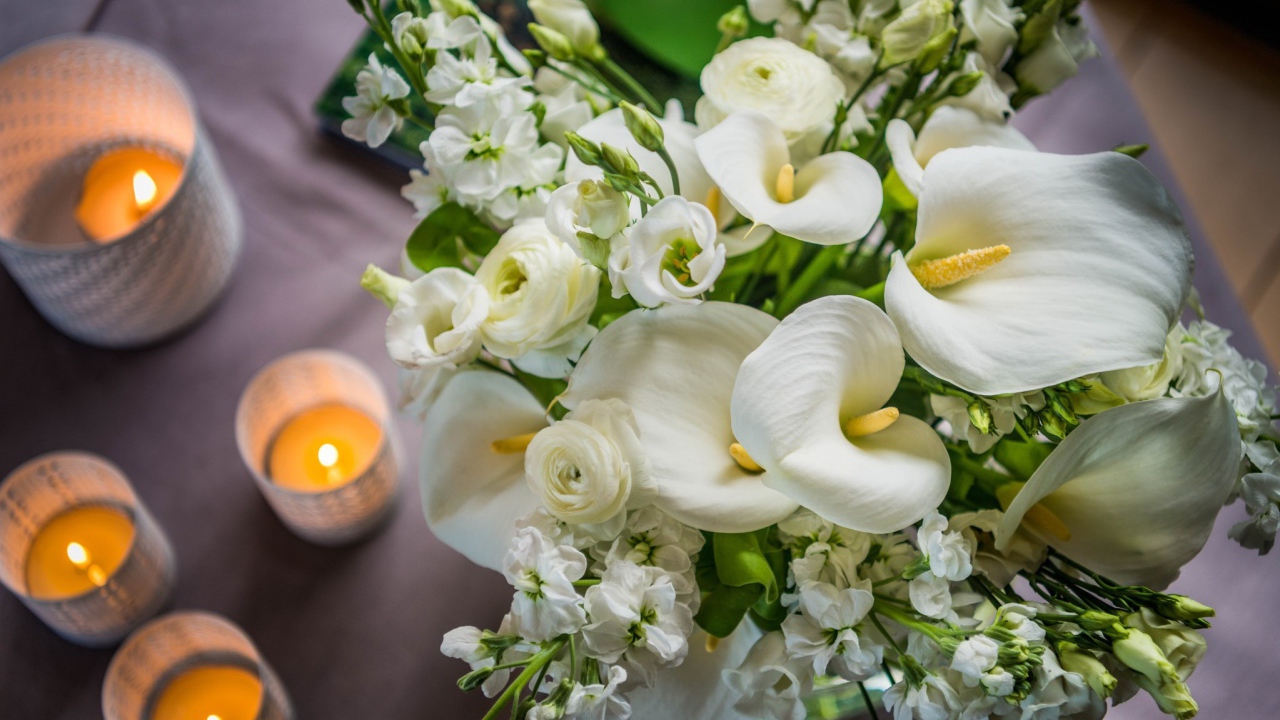 Букет белых цветов зантедеския и левкой с зажженными свечами на столе