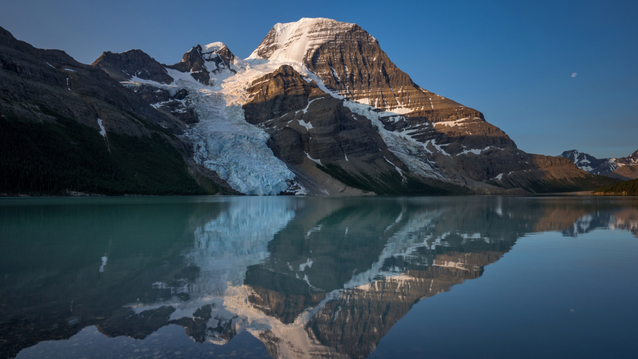 Гора в снегу отражается в водной глади озера 